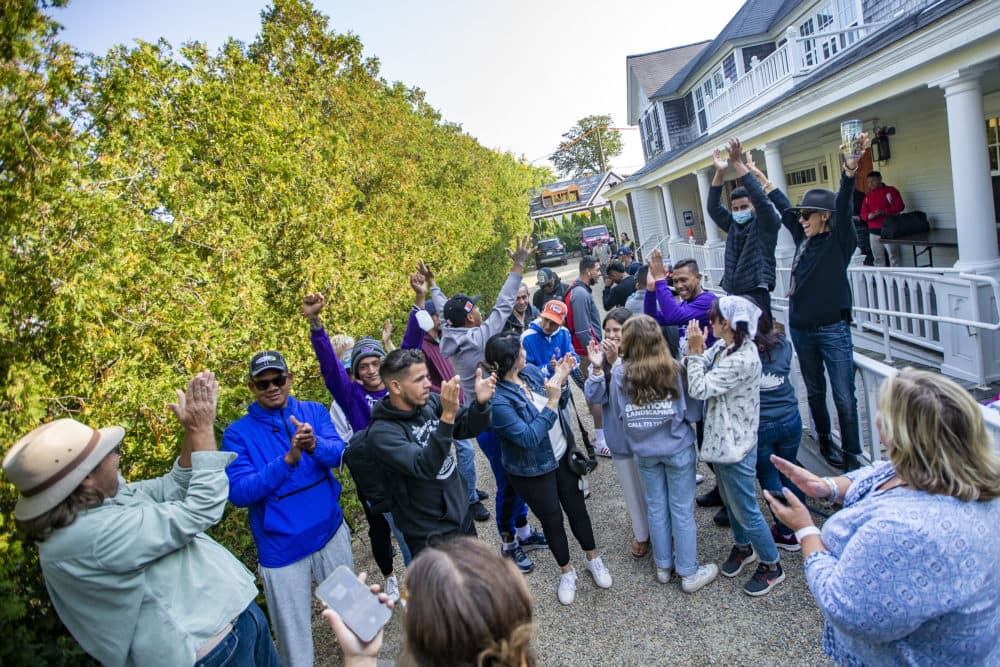 Volunteers and immigrants cheer in the driveway of St. Andrews Parish House as the buses arrive to take them to the ferry to leave Martha’s Vineyard. (Jesse Costa/WBUR)