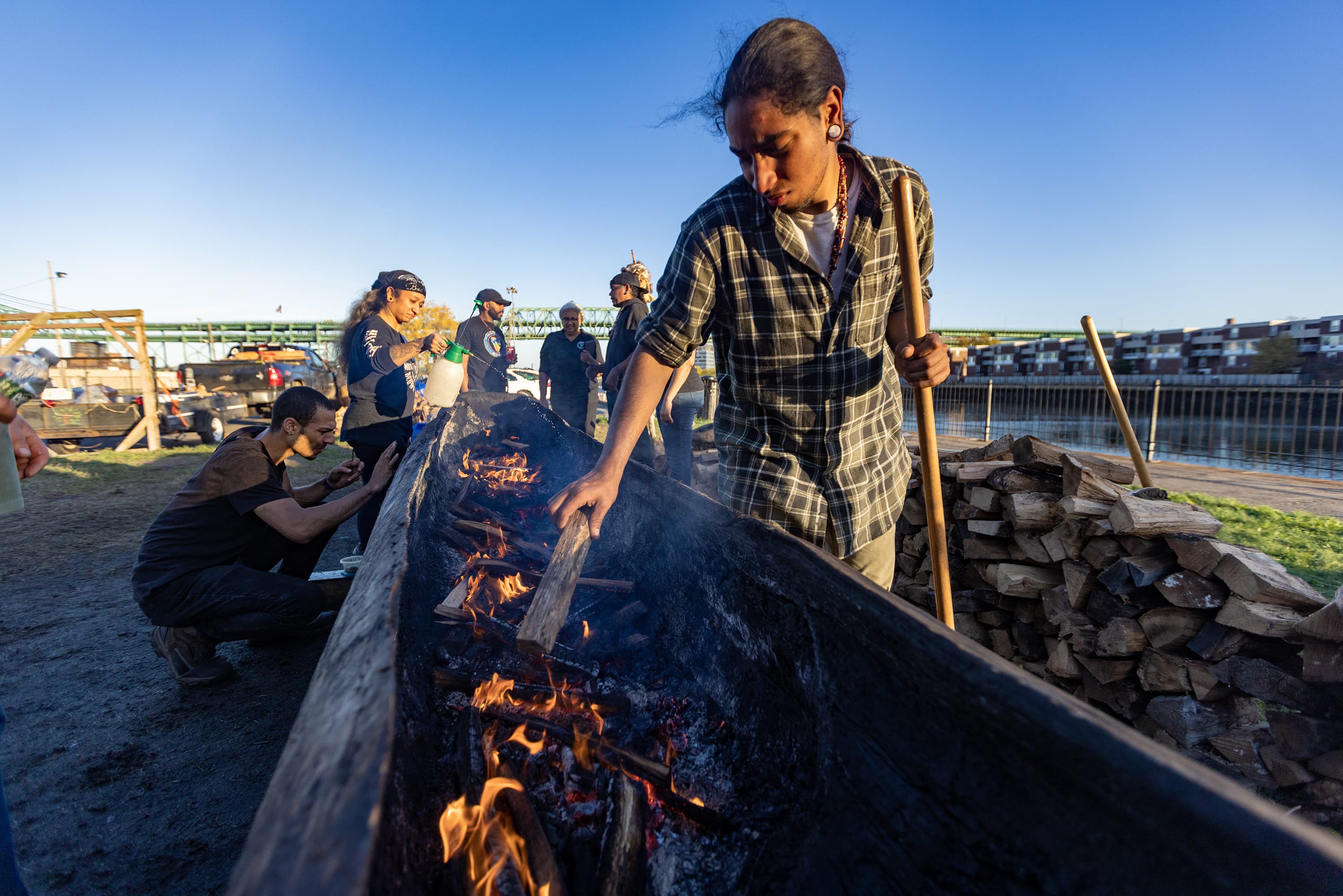 Daishuan Red Deer Garate, a cultural apprentice of the Nipmuc tribe, places wood pieces into the fire during the burning of a traditional mishoon at the Charlestown Little Mystic Boat Slip. (Jesse Costa/WBUR)