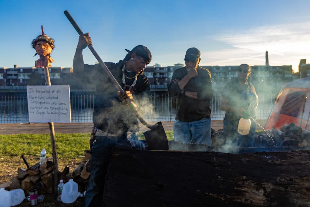 Andre StrongBearHeart tends to the fire while burning a traditional mishoon. A sign posted beside the worksite reads &quot;In the memorial of all Northeast Woodland Indigenous, who were murdered and beheaded by the English for public display.&quot; (Jesse Costa/WBUR)