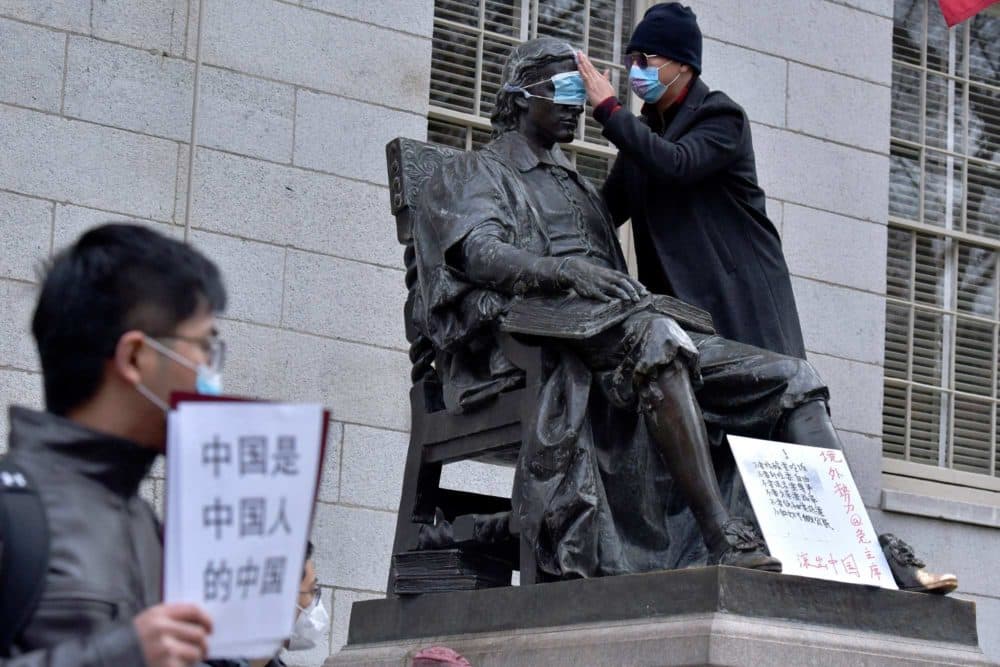 A man places a mask over the eyes of the John Harvard Statue in Harvard Yard as dozens of students and faculty demonstrate against strict anti-virus measures in China, on Tuesday at Harvard University. (Josh Reynolds/AP)