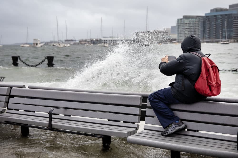 Brooks Payne shoots a video of waves washing across Long Wharf in Boston at high tide during the storm on Dec. 23. (Robin Lubbock/WBUR)