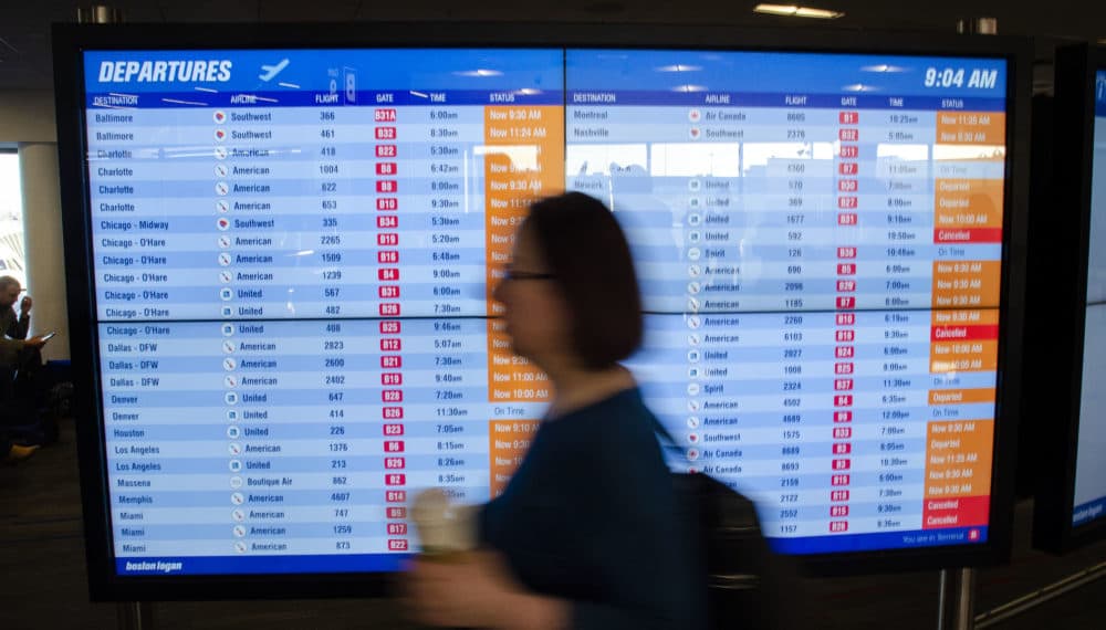 A traveler walks past a departures board filled with delayed and canceled domestic flights at Logan Airport's Terminal B. (David Lubbock for WBUR)