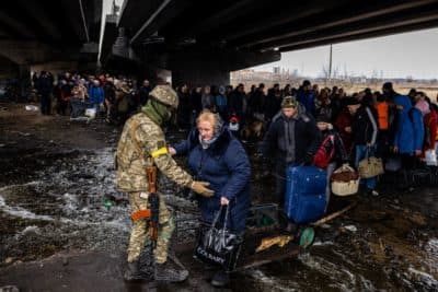A Ukrainian serviceman helps evacuees gathered under a destroyed bridge, as they flee the city of Irpin, northwest of Kyiv, on March 7, 2022. - Ukraine dismissed Moscow's offer to set up humanitarian corridors from several bombarded cities on March 7, 2022, after it emerged some routes would lead refugees into Russia or Belarus. The Russian proposal of safe passage from Kharkiv, Kyiv, Mariupol and Sumy had come after terrified Ukrainian civilians came under fire in previous ceasefire attempts. (Photo by Dimitar DILKOFF / AFP) (Photo by DIMITAR DILKOFF/AFP via Getty Images)