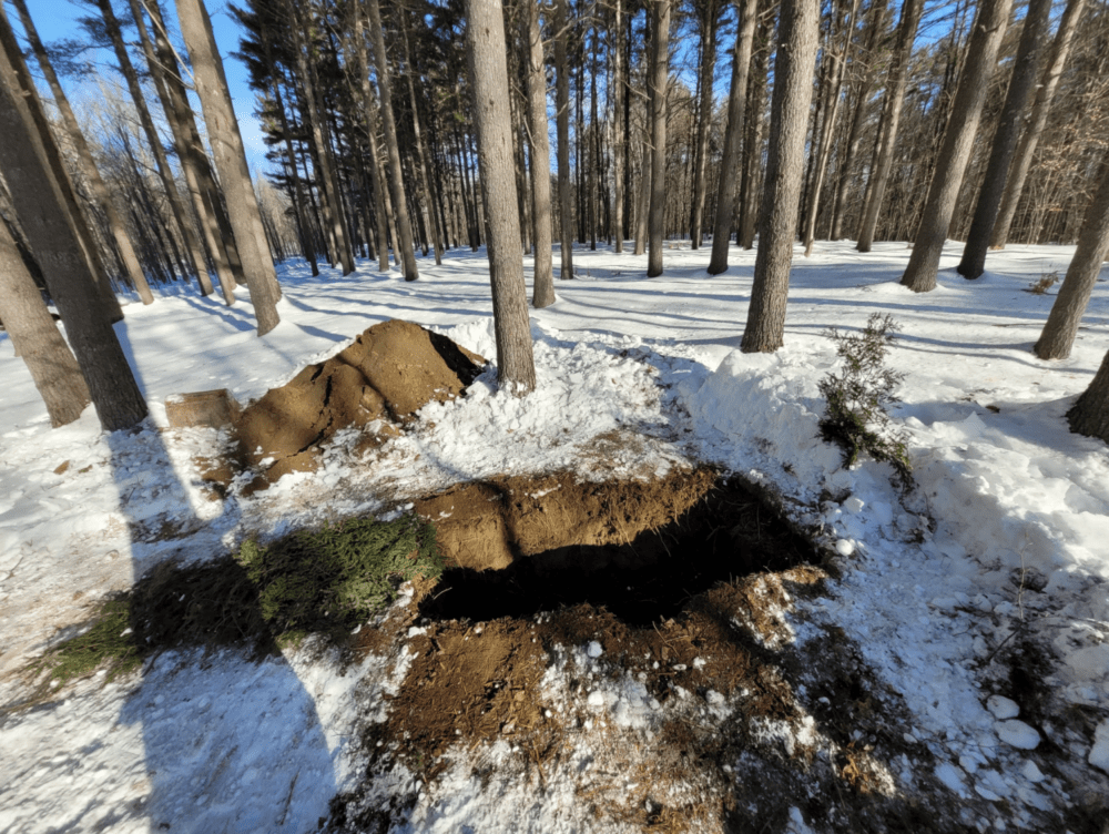 A grave dug for a green burial at the Baldwin Hill Conservation Cemetery in Fayette, Maine in January 2023. It's about 30 inches deep and pine boughs are laid in and alongside the grave. No concrete vault, steel or rare wood casket, or embalming chemicals are used at this cemetery. (Tyler Keniston/Kennebec Land Trust)