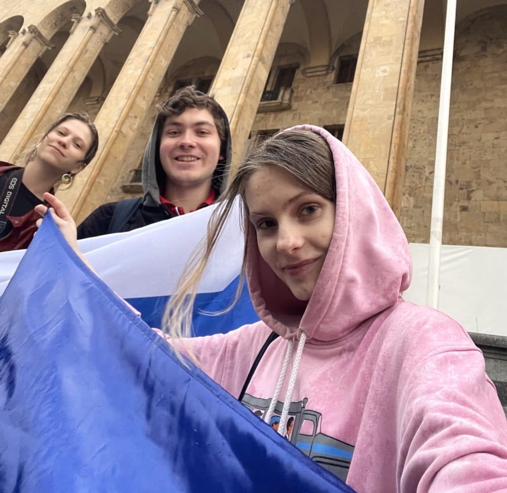 Russian YouTubers Natasha and Zack attending an anti-war rally with a friend in Tbilisi, Georgia. They are holding Russian white-blue-white flags which symbolize resistance to the country's war in Ukraine. The flag's design replaces the red stripe on Russia's national flag with a white one. The colors represent peace, truth, and justice; they are also a nod to the Novgorod Republic, a proto-democratic state that existed during Russia's medieval period. (Courtesy Natasha Kurnaeva)