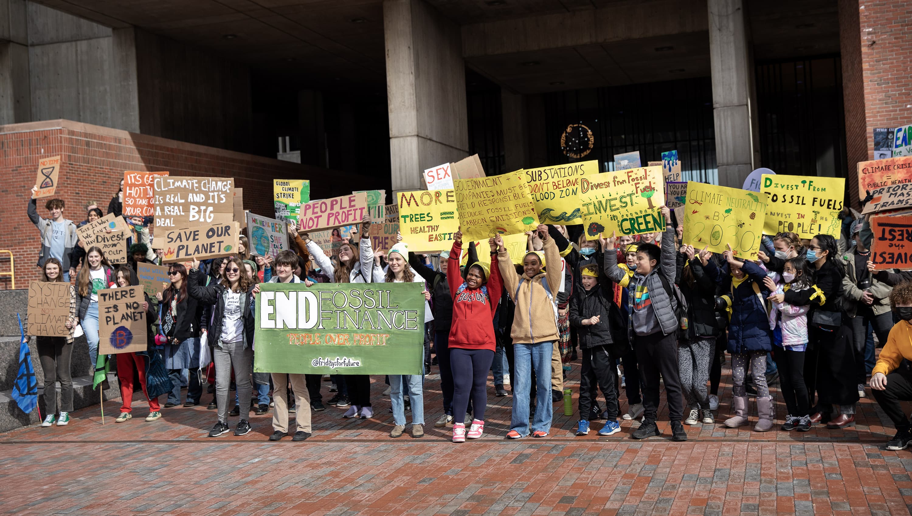 Fridays For Future protesters demanding a halt to all investment in fossil fuels, hold up their banners in front of Boston City Hall. (Credit: Robin Lubbock/WBUR)