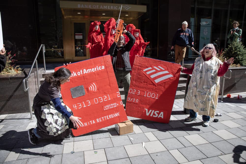 Protesters chop up a giant credit card with a solar powered chainsaw in front of the Bank of America in downtown Boston. (Credit: Robin Lubbock/WBUR)