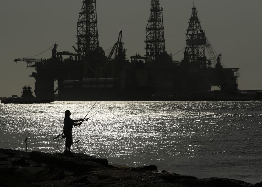 A man wears a face mark as he fishes near docked oil drilling platforms. (Eric Gay/AP)
