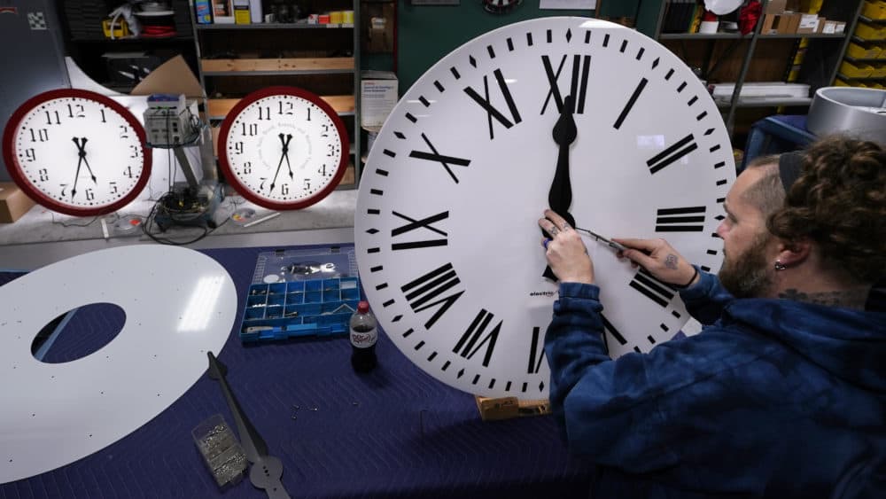 Ian Roders fastens the hands to a clock at Electric Time Company, Nov. 1, 2022, in Medfield (Charles Krupa/AP)