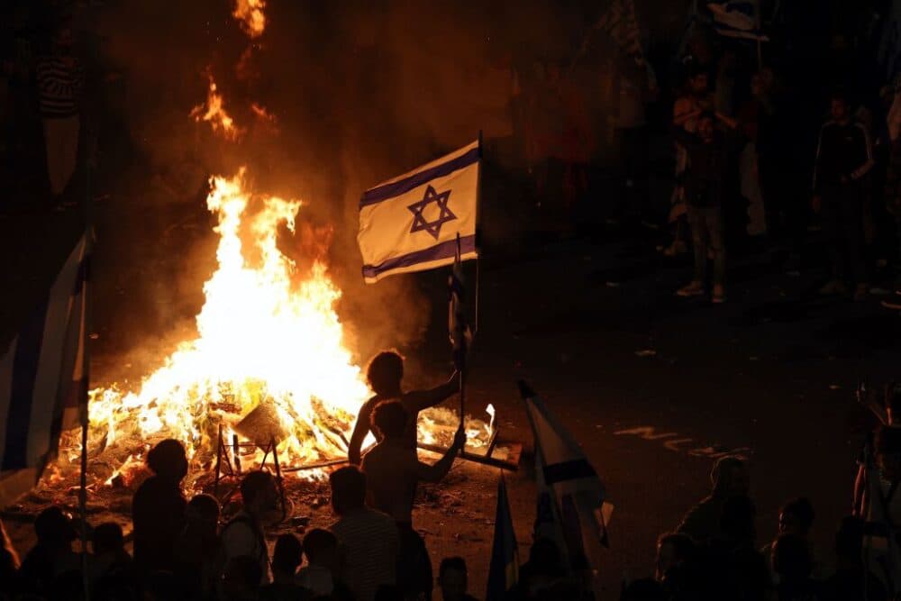 Protesters block a road and hold national flags as they gather around a bonfire during a rally against the Israeli government's judicial reform in Tel Aviv, Israel on March 27, 2023. AHMAD GHARABLI/AFP via Getty Images)