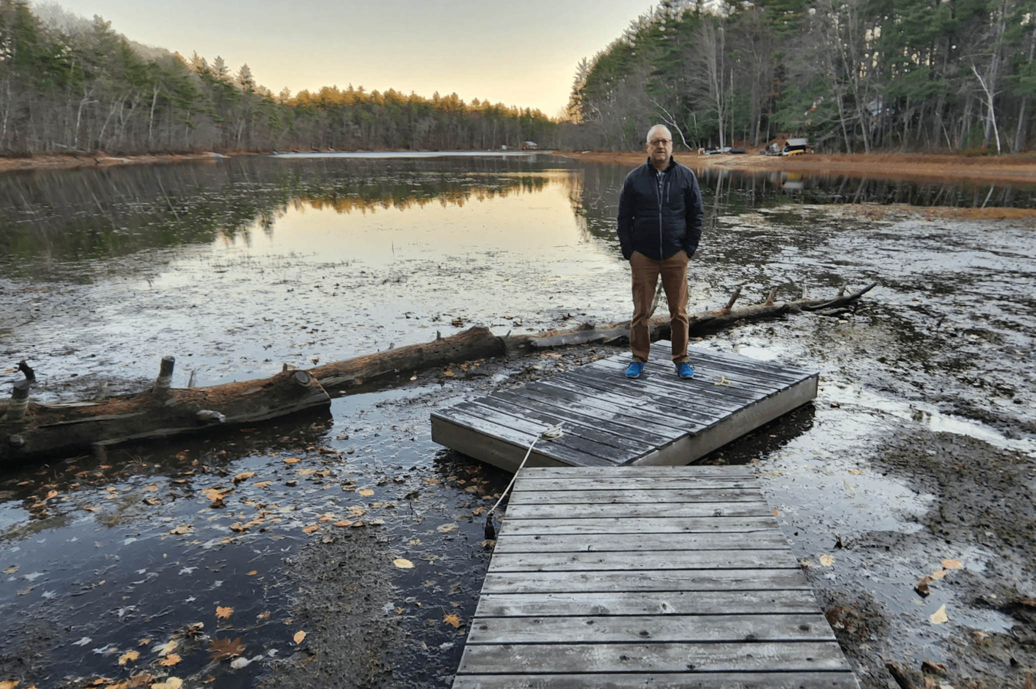 Jim Metivier stands on extensions of his dock over Long Pond in Denmark, Maine, in Nov. 2022. Water levels on his property have gradually receded over a period of several years. &quot;I haven't been able to get my canoe out since July,&quot; Metivier said. (Susan Sharon/Maine Public)