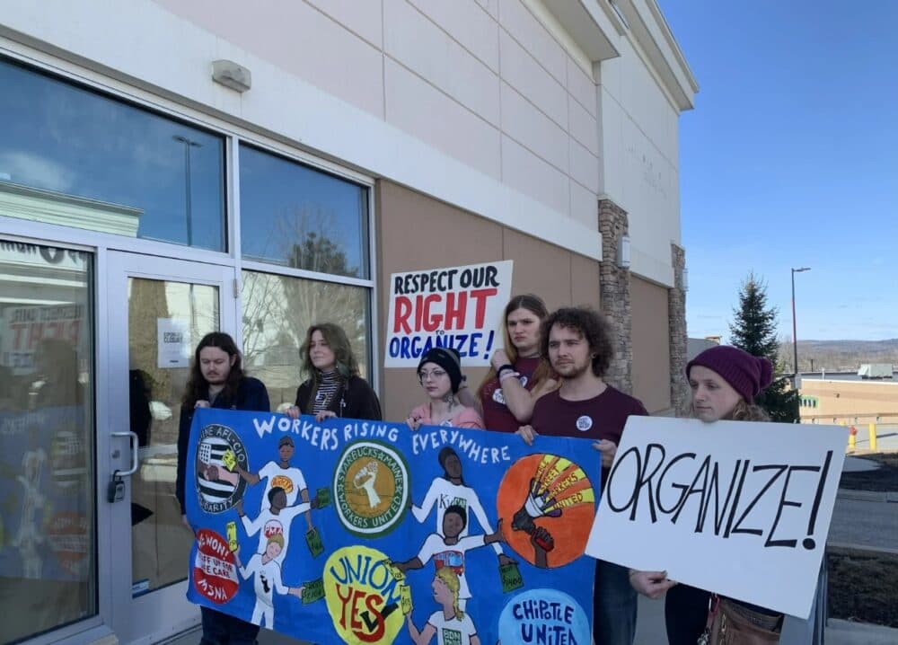 Former employees of Chipotle Mexican Grill in Augusta celebrate the settlement agreement they reached with the restaurant chain. They spoke outside the shuttered store, which had been closed for more than seven months, on March. 27. (Nicole Ogrysko/Maine Public)