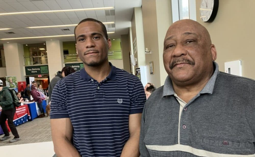 Preston Reid, 38, stands with his father, Pershing Reid, 72, at a job fair in Greenfield, Massachusetts. Pershing Reid is looking for a job driving a van or a bus, but he doesn't have the digital skills to submit an application online, so his son assists him. (Nancy Eve Cohen/NEPM)