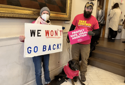 Nancy Brennan of Weare, Curtis Register of Dover and Register's dog Lord Remington demonstrate in support of abortion rights at the New Hampshire State House Wednesday, Feb. 15. (Paul Cuno-Booth/NHPR)