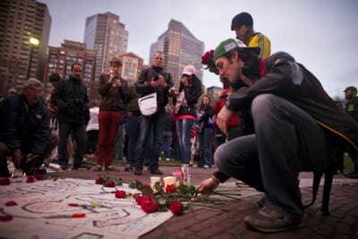 Matt Onorato lays flowers on a banner during a candle light vigil at the Boston Common April 16, 2013, a day after the Boston Marathon bombing. (Dominick Reuter for WBUR)