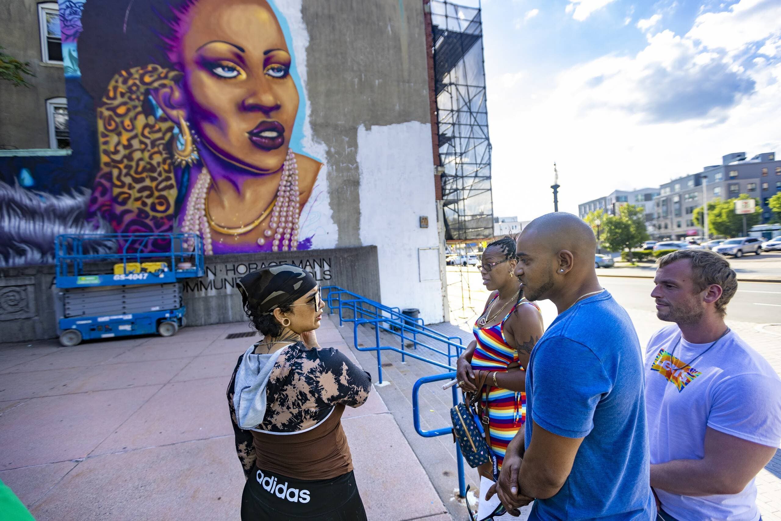 Taufiq Chowdhury and Kim Hester speak with artist Rixy in front of the Allston mural &quot;Rita's Spotlight,&quot; honoring the memory of Rita Hester. Street Theory helped install this mural in the neighborhood. (Jesse Costa/WBUR)