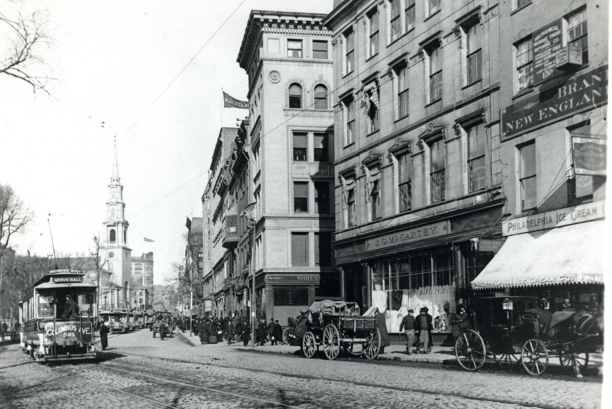 A black and white photograph with a trolley car from the late 1800s traveling along a city street.