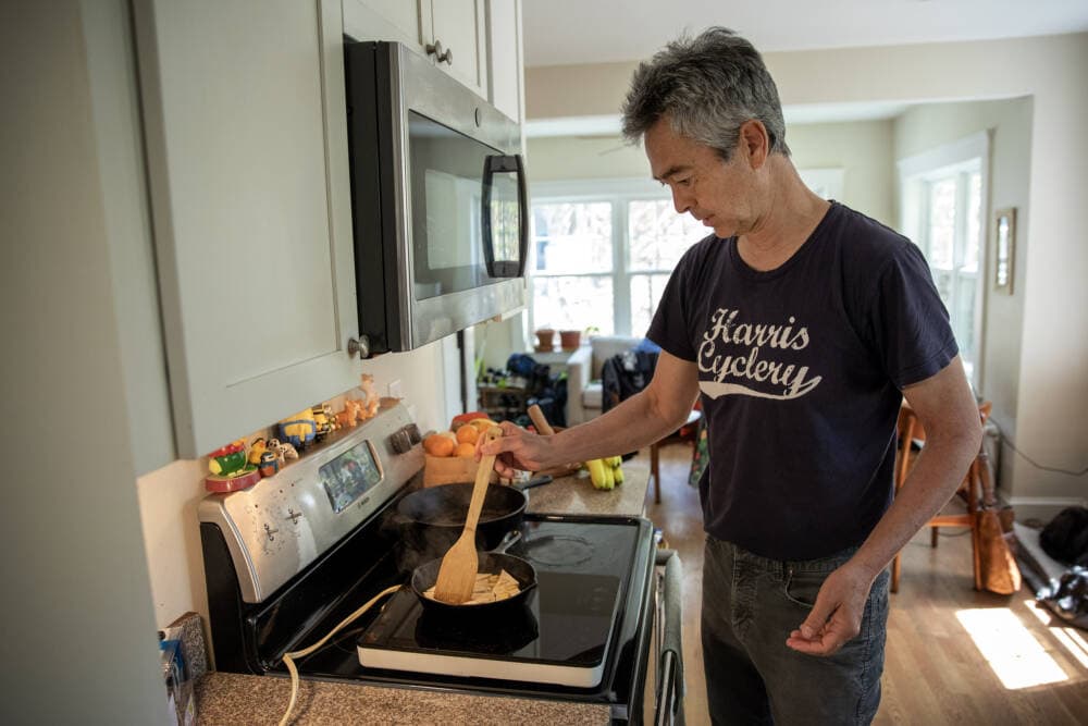 Nathan Phillips has his induction cooker placed on top of his conventional range as he cooks tofu with garlic and broccoli. (Robin Lubbock/WBUR)