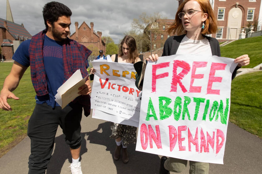 Kirin Kowalski (left), Amina Mednicoff-Misra (center), and Anna Tjeltveit (right), members of The Wesleyan Democratic Socialists, distribute signs to inform the student body that the University agreed to meet their demands to cover healthcare costs related to abortion. (Greg Miller/Connecticut Public)