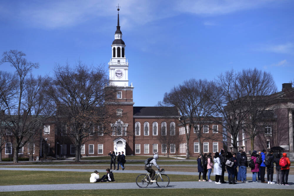 A bicyclist passes a college tour group outside the Baker Library on Dartmouth Green at Dartmouth College, Friday, April 7, 2023, in Hanover, N.H. The college announced in March 2023 that it housed partial Native American skeletal remains in their collection. Dartmouth has set in motion an effort to repatriate the remains to the appropriate tribes. (Charles Krupa/AP)