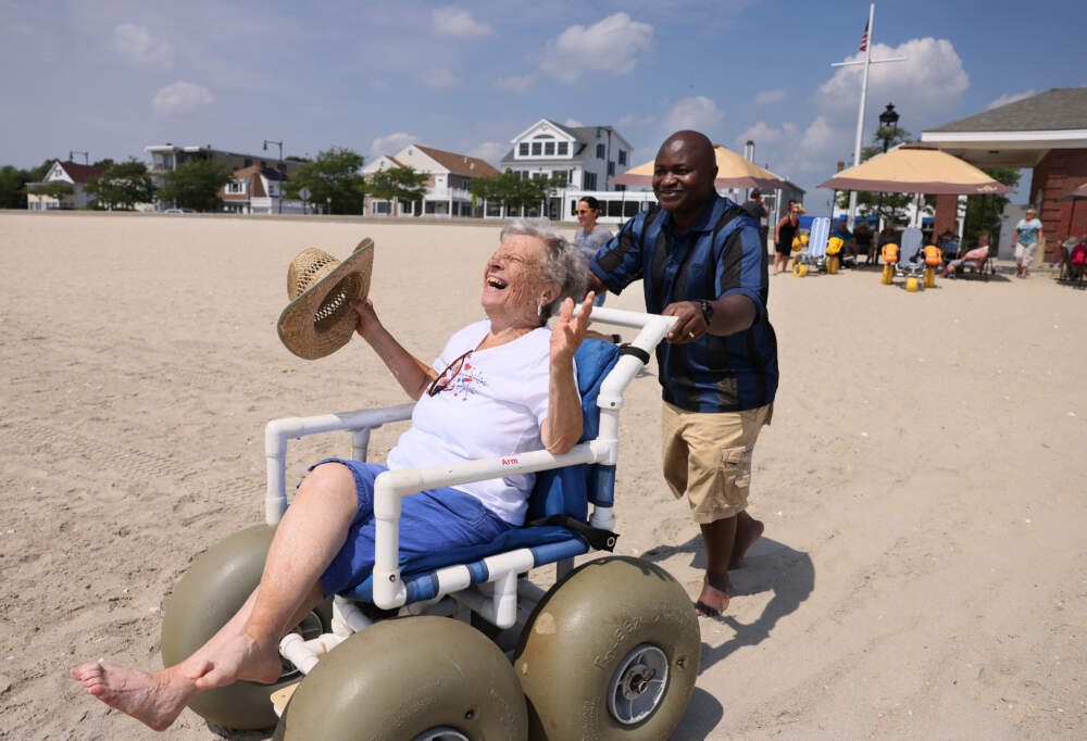 Diane Weinstein, 82, throws her head back and laughs as Ansu Kinteh helps to wheel her toward the ocean as she and other residents of the Cohen Florence Levine Estates assisted living center spend a day at Revere Beach. (Jessica Rinaldi/The Boston Globe via Getty Images)