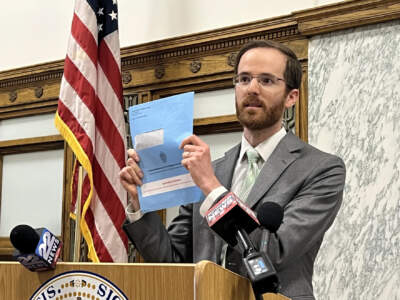 Mike Levine, assistant secretary for MassHealth, holds up an envelope many Medicaid recipients could be receiving. The documents ask for more information to help determine if a person is eligible to continue receiving benefits. (Adam Frenier/NEPM)