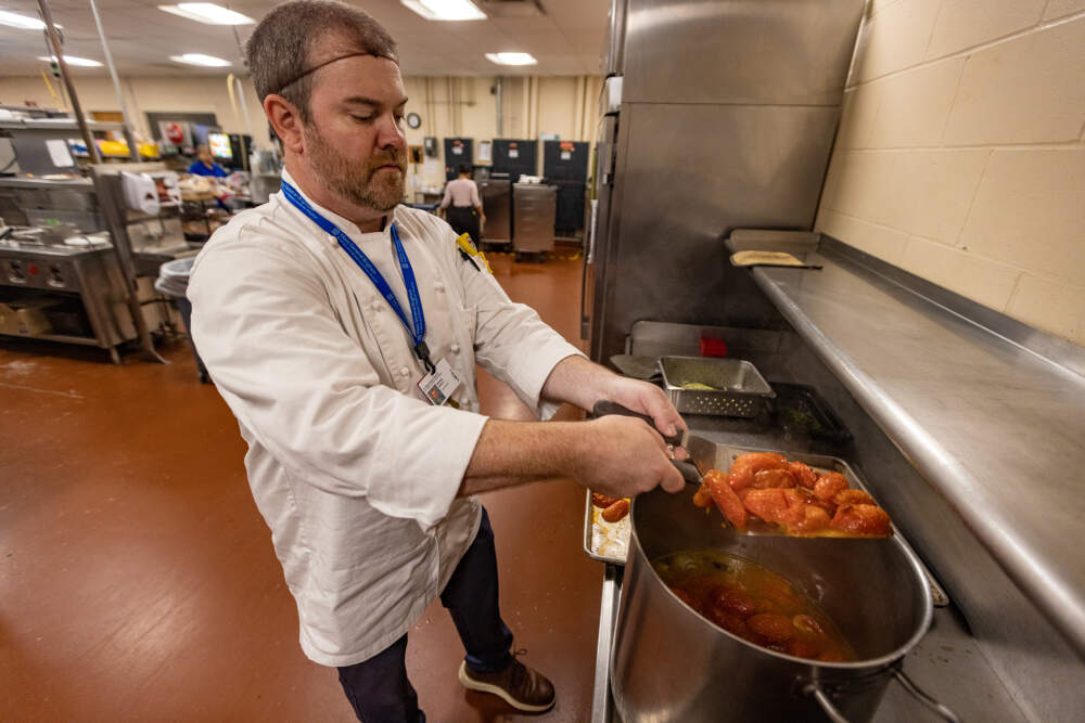 Mike Hanley, general manager of food services at Faulkner Hospital, places roasted tomatoes into a pot as he prepares roasted tomato and shallot coulis. (Jesse Costa/WBUR)