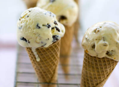 White ice cream with dark speckles melt in a waffle cone on a stand.