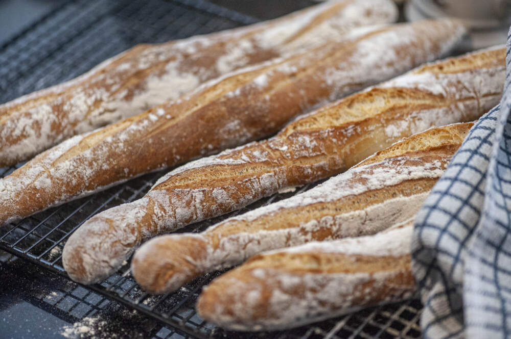 A close-up three quarter view of freshly baked baguettes, cooling on a wire rack with a tea towel to the right. (Getty Images)