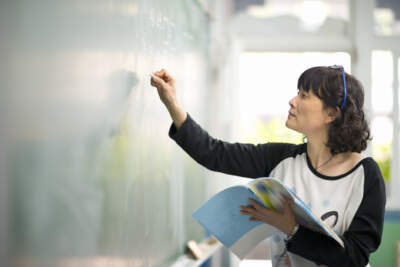 As Asian American teacher writes on the chalkboard at the front of a classroom. (Getty Images)