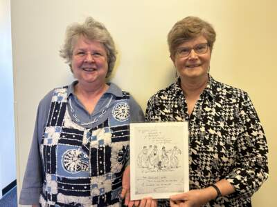 Suzanne Gall-Marsh, of the Friends of the Boston Harbor Islands, and author Stephanie Schorow pose with a line drawing of the Merrie Trippers. (Amanda Beland/WBUR)