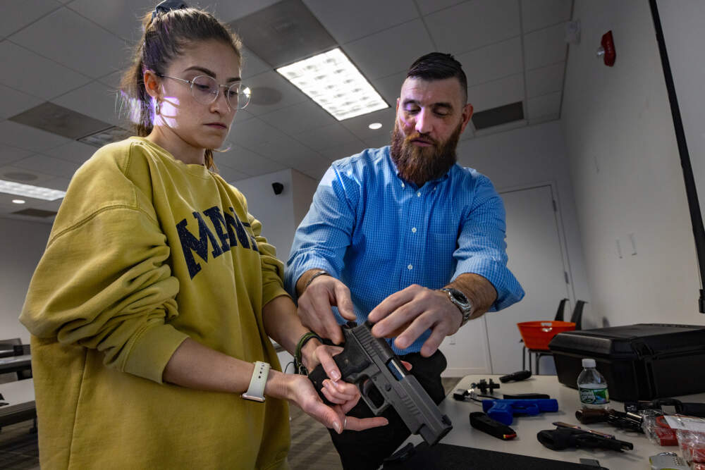 Army veteran and firearms safety instructor Kevin Lambert shows Maeve Cardwell how to safely hold a handgun as part of the program at William James College. (Jesse Costa/WBUR)
