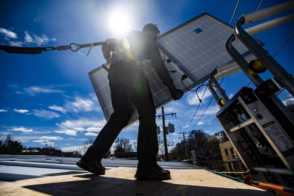 A technician removes a solar panel from a lift  during a solar panel installation on the rooftop of Boston Building Resources in Jamaica Plain. (Jesse Costa/WBUR)