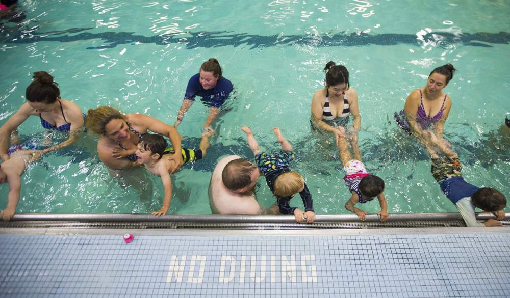 Toddlers are instructed to kick their legs in the water while holding onto the wall. (Jesse Costa/WBUR)