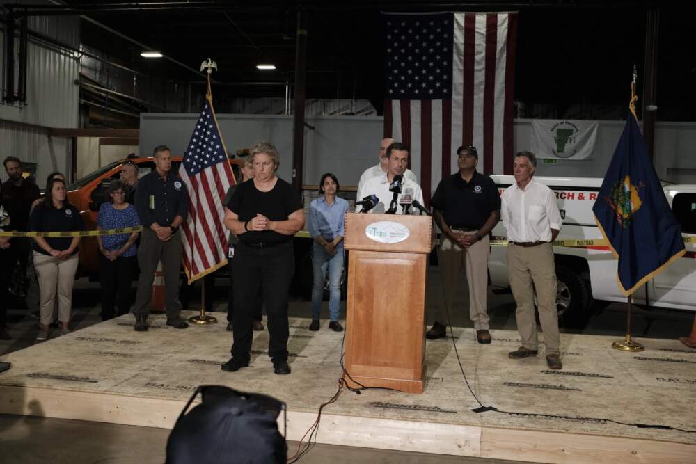U.S. Transportation Secretary Pete Buttigieg speaks at a press conference flanked by officials including Rep. Becca Balint, in blue, and Gov. Phil Scott, on right. (Joey Palumbo/Vermont Public)