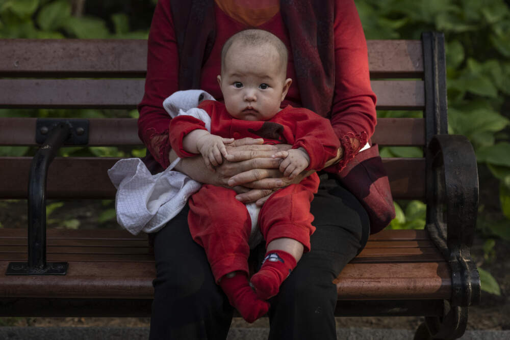 A woman holds a baby at a lush local park. (Kevin Frayer/Getty Images)