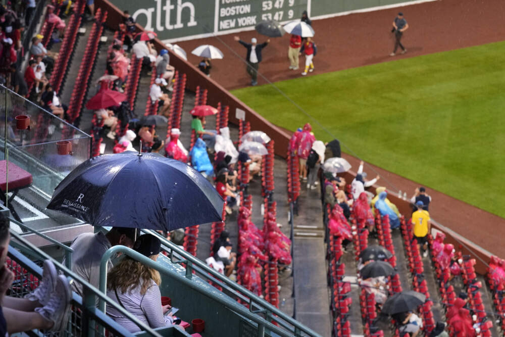 Two fans wait under an umbrella during a rain delay before a baseball game between the Boston Red Sox and the Atlanta Braves at Fenway Park, Tuesday, July 25, 2023, in Boston. (AP Photo/Charles Krupa)