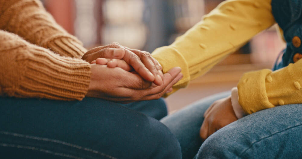 Two people hold hands while sitting together. (Getty Images)