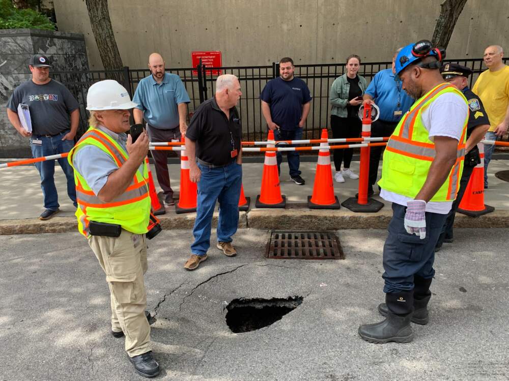 A small crowd gathers to observe a sinkhole on Longwood Avenue in Boston, just outside Children's Hospital, while Boston workers check out what happened. (Robin Lubbock/WBUR)