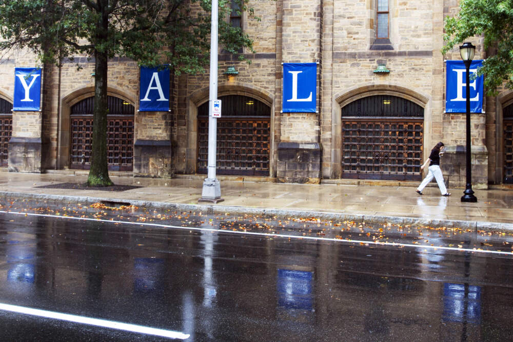 A woman walks by a Yale sign reflected in the rainwater on the Yale University campus in New Haven, Conn. (Ted Shaffrey/AP)
