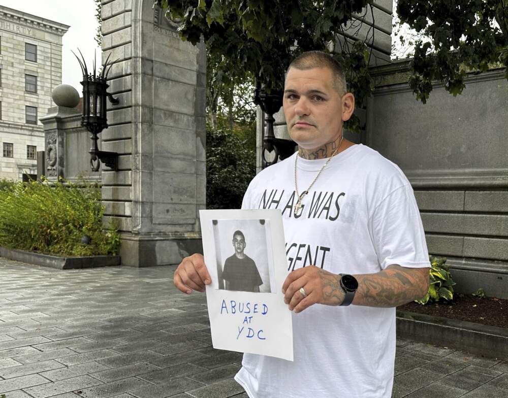 Michael Gilpatrick holds a copy of his intake photo from New Hampshire's youth detention center as he and other former residents of the Youth Development Center, now called the Sununu Youth Services Center, hold a rally outside the Statehouse in Concord, Friday, Aug. 25, 2023, to press for a federal investigation into their claims of physical and sexual abuse. (Holly Ramer/AP)