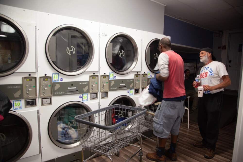Maurice Boowa (left) and Jim Chase (right) chat while doing their laundry at Wash Street in Manchester where, twice a week, unhoused people have the opportunity to clean their clothes. (Gabriela Lozada/NHPR)