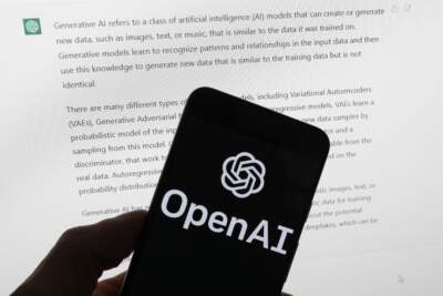 The OpenAI logo is seen on a mobile phone in front of a computer screen displaying output from ChatGPT. (Michael Dwyer/AP)