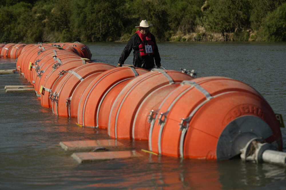 A kayaker walks past large buoys being used as a floating border barrier on the Rio Grande, Aug. 1, 2023, in Eagle Pass, Texas. A federal judge on Wednesday, Sept. 6, ordered Texas to move a large floating barrier to the riverbank of the Rio Grande after protests from the the U.S. and Mexican governments over Republican Gov. Greg Abbott’s latest tactic to stop migrants from crossing America’s southern border. (Eric Gay/AP)