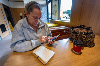 Sitting inside a McDonald's, Brenda Banville makes a phone call to look for an apartment. She spends much of her time at the fast-food restaurant as she waits for her son to return from making DoorDash deliveries. (Jesse Costa/WBUR)
