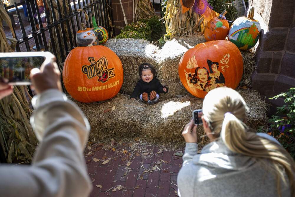 A baby looks up and laughs while her mother (left), and aunt take photographs outside the Salem Witch Museum. (Jesse Costa/WBUR)