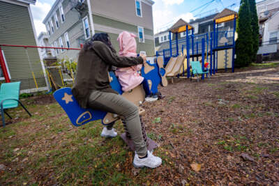 A mother plays with her two-year-old daughter on an airplane spring rocker in the play yard at the family shelter where they are staying. (Jesse Costa/WBUR)
