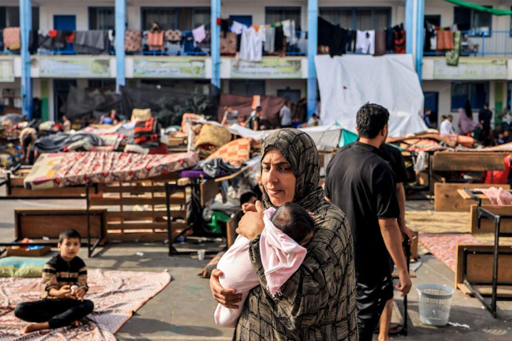 A woman walks carrying an infant in the playground of a school run by the United Nations Relief and Works Agency for Palestine Refugees (UNRWA) agency that has been converted into a shelter for displaced Palestinians in Khan Yunis in the southern Gaza Strip on Oct. 25, 2023, amid the ongoing battles between Israel and the Palestinian group Hamas. (Mahmud Hams/AFP via Getty Images)