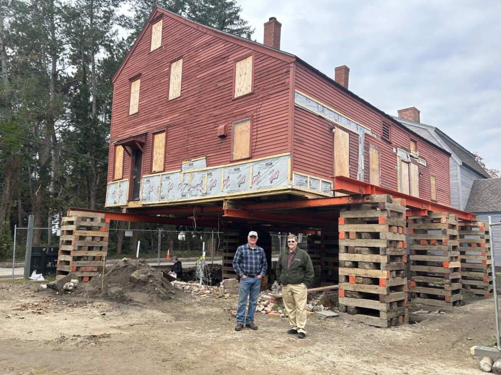 Rodney Rowland and Arron Sturgis stand in front of the Penhallow House, on the day it was raised into the air. The house will come back down after a new climate-resilient foundation is installed. (Mara Hoplamazian/NHPR)