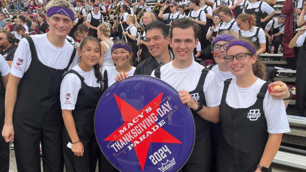UMass Amherst Chancellor Javier Reyes poses with members of the Minutemen Marching Band. The band will be performing in the Macy's Thanksgiving Day Parade in 2024. (Elizabeth Román/NEPM)